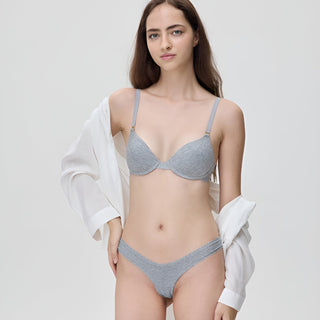 Woman wearing a gray bra and underwear set with a white shirt over her shoulders on a light gray background