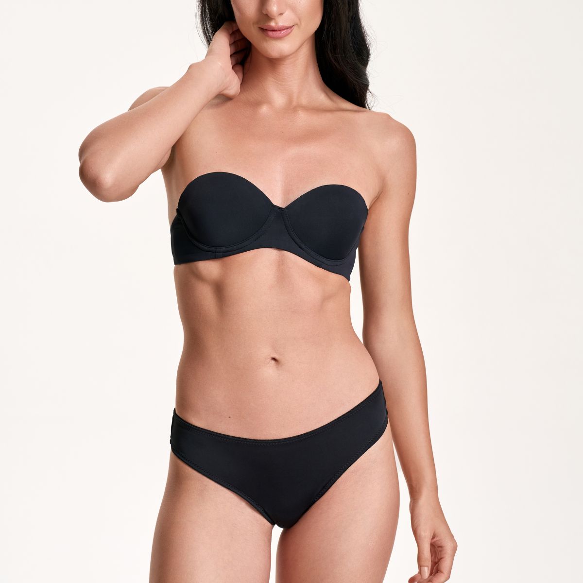 Woman wearing a black strapless bikini against a plain background