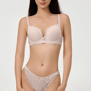 Woman wearing a light pink lace bra and panties set on a white background