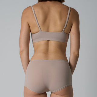 Person wearing a beige bra and panties set against a gray background