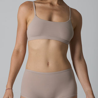 Person wearing a beige bra and underwear set on a gray background