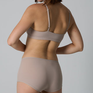 Person wearing a beige bra and underwear set on a gray background