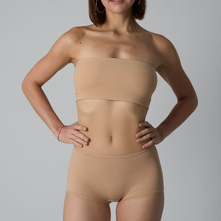 Woman wearing a beige strapless top and high-waisted leggings against a gray background