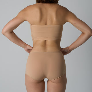 Person wearing a beige strapless top and high-waisted underwear set on a gray background