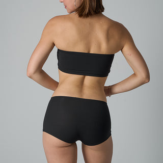 Person wearing a black strapless top and high-waisted bikini bottom on a gray background