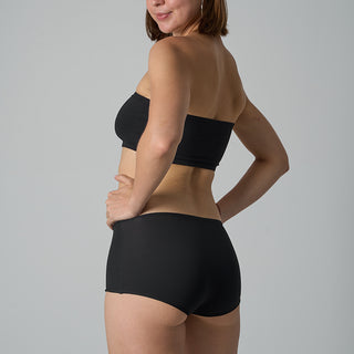 Person wearing a black strapless top and black high-waisted underwear on a gray background