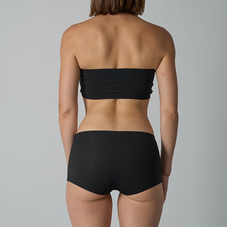 Person wearing a black strapless top and black high-waisted bikini bottom on a gray background