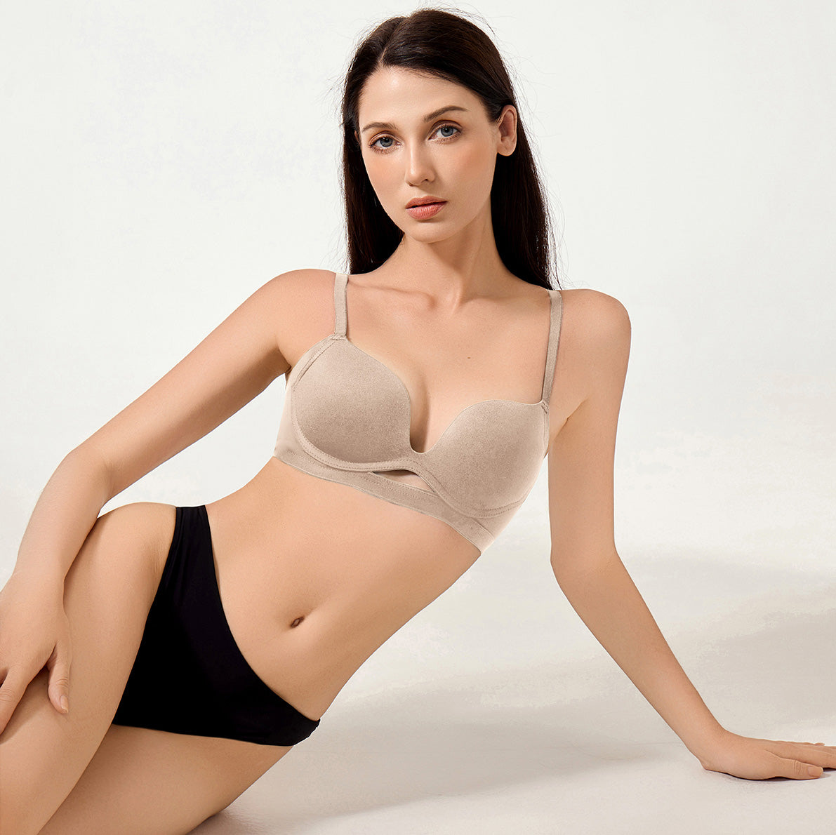 Woman wearing a beige bra and black underwear on a white background