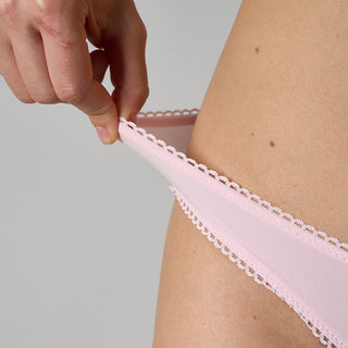 Person wearing a pink lace-trimmed underwear against a gray background